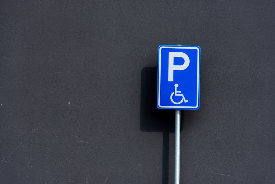 A close-up view of a parking lot surface with designated handicapped accessible parking spaces marked by white lines and symbols. The asphalt is dark and textured, with multiple parking bays visible, each outlined with clean, crisp white paint. The prominent wheelchair symbol is displayed in the foreground within a rectangular border, indicating accessible parking. In the background, additional parking spaces are outlined, showing the organized layout of the lot. The scene highlights the well-maintained infrastructure designed for easy access, which could be relevant to a home relocation or moving service like Man with Van Yeading, that requires careful planning around parking and access points for furniture transport and loading during house moves.